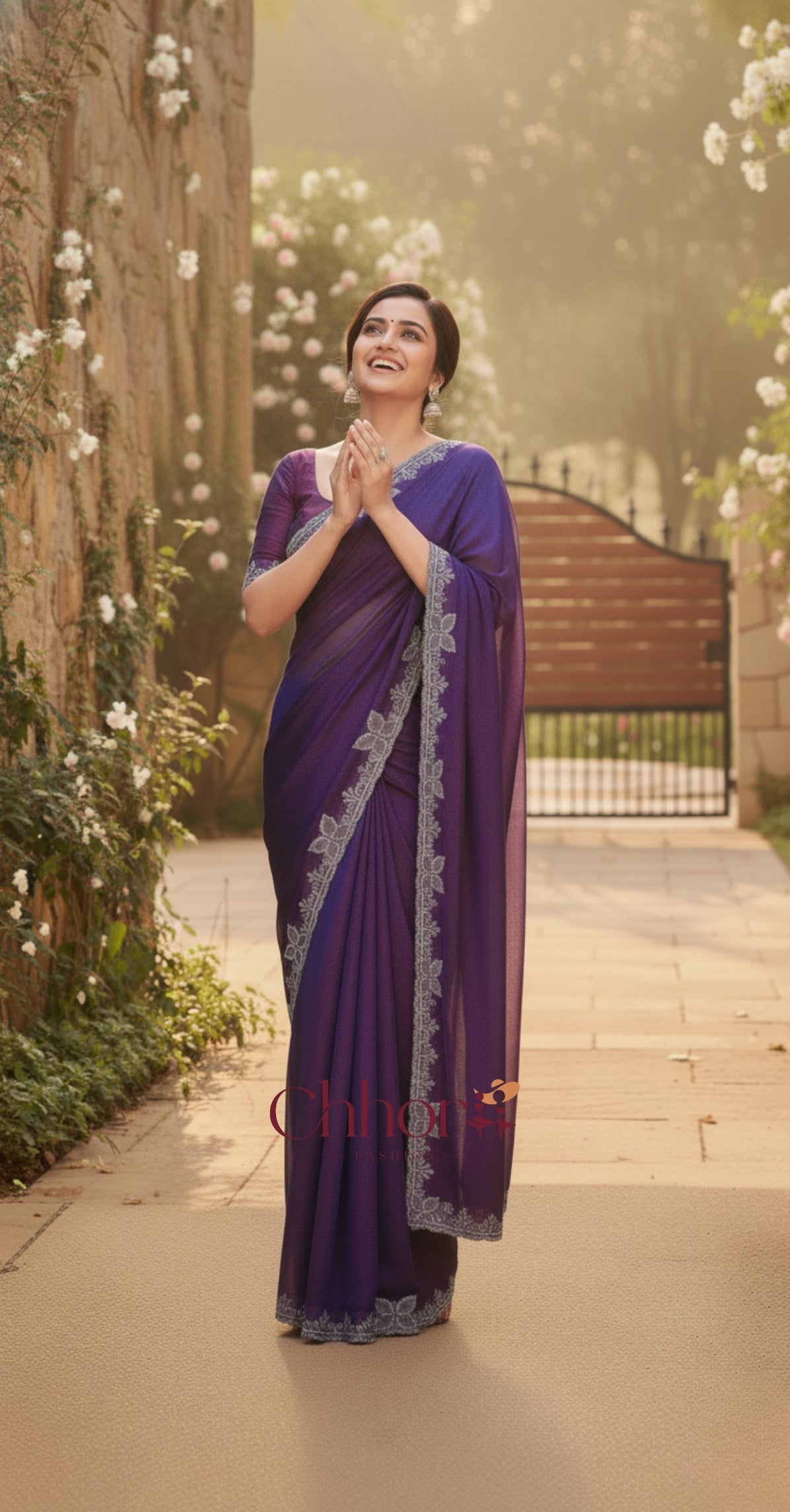 Woman in a purple saree standing in a garden with flowers and a wooden gate in the background | Chhorii Fashion